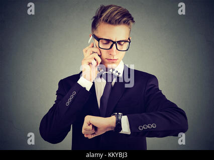 Business e la gestione del tempo concetto. imprenditore guardando orologio da polso, parlando al telefono cellulare. Foto Stock