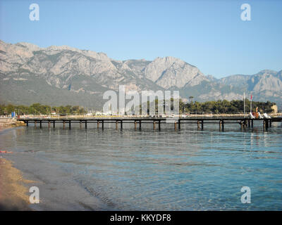 Kemer Antalia bella vista sul mare. Spiaggia Kemer Antalia con sabbia e montagne, il mare con la nave. Bellissimo porto vicino alla spiaggia di sabbia. Foto Stock