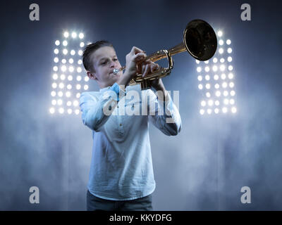 Ragazzo suonare la tromba con blu umore fendinebbia e luci da palco in background Foto Stock