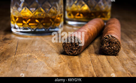 Due sigari cubani con due bicchieri di whiskey su un vecchio tavolo di legno con uno sfondo sfocato Foto Stock