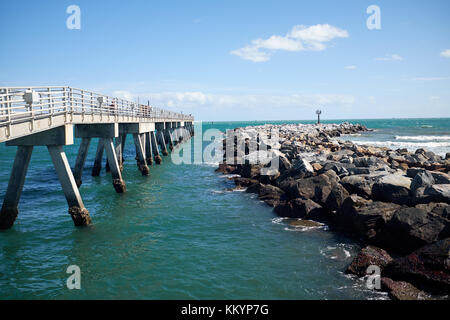 Roccia Naturale frangiflutti e di una parte delle difese costiere o la parete di un piccolo porto, al fianco di un molo proteso in un mare calmo in una vista sfuggente Foto Stock