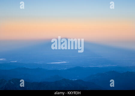 Sunrise dietro un picco di montagna con la sua ombra proiettata sulla vallata tra la Svizzera (Valais) e Italia Foto Stock