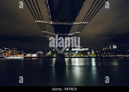 Una lunga esposizione shot prese sotto il Millennium Bridge sul fiume Tamigi a Londra presso moody notte Foto Stock
