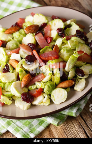 Insalata fresca di cavoli di Bruxelles di mirtilli rossi secchi, mandorle e prosciutto close-up su una piastra verticale. Foto Stock