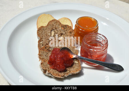 Tre pezzi di domestici, pane fatto in casa con grano intero e piccoli vasetti con gustose fragole e marmellata di albicocche Foto Stock