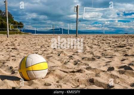 La pallavolo si trova sulla spiaggia di sabbia con tribunali vuoti in background Foto Stock