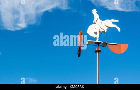 In legno cavallo bianco e cowboy banderuola con il rosso delle palette di turbina sotto il cielo blu Foto Stock