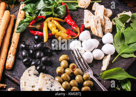 Antipasti misti i peperoncini sott'aceto, olive e mozzarella servita su cast-ferro da stiro su un tavolo di legno con forcella vintage. Foto Stock