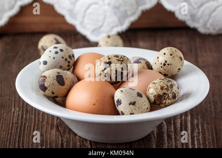 Quaglia e le uova di gallina in piastra bianca sul vecchio tavolo in legno Foto Stock