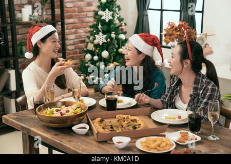 Happy amici indossando cappelli di Babbo Natale e la condivisione di pizza insieme nella parte anteriore dell'albero di Natale Foto Stock