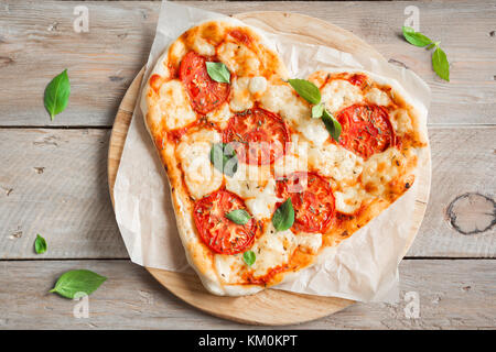 A forma di cuore la pizza margherita su sfondo di legno con copia spazio. pizza con pomodoro, mozzarella e basilico per il giorno di San Valentino. Foto Stock