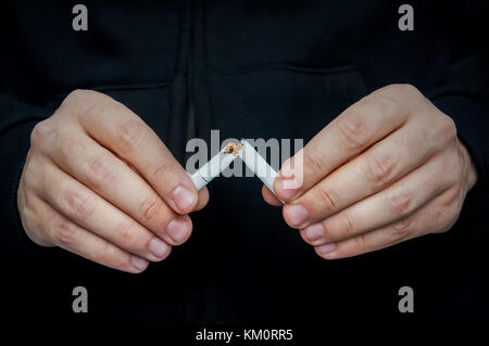 Smettere di fumare - Maschio lato la frantumazione di sigaretta su uno sfondo nero. anti-tabacco concetto. Foto Stock