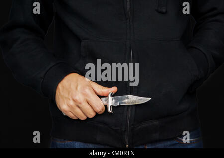 Un tossicodipendente scassinatore in una felpa con cappuccio nero. la nozione di delitto di rapina. primo piano di un giovane uomo di mano, tenendo un coltello, per attaccare, Foto Stock