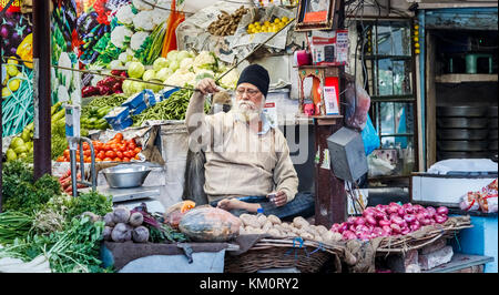 Maschio locale stallholder Sikh seduto a gambe incrociate in un negozio di vegetali, Amritsar e una città nel nord-occidentale dell'India nella regione di Majha del Punjab Foto Stock