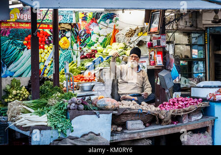 Maschio locale stallholder Sikh seduto a gambe incrociate in un negozio di vegetali, Amritsar e una città nel nord-occidentale dell'India nella regione di Majha del Punjab Foto Stock