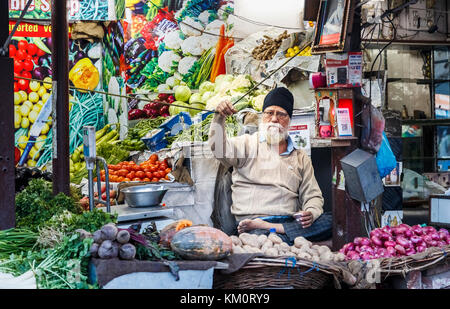 Maschio locale stallholder Sikh seduto a gambe incrociate in un negozio di vegetali, Amritsar e una città nel nord-occidentale dell'India nella regione di Majha del Punjab Foto Stock