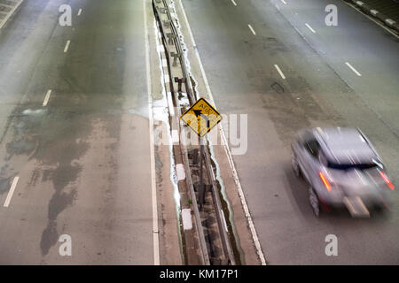 Auto passando da un graffito che legge in portoghese "atteggiamento", spruzzato sulla scheda gialla a sinistra del traffico di segnalazione segno, Sao Paulo, Brasile Foto Stock