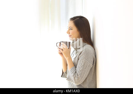 Vista laterale verticale di un grave pensieroso donna che guarda lontano tenendo una tazza di caffè isolato su bianco su un lato Foto Stock