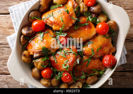 Cosce di pollo arrosto con castagne e i pomodori in una ciotola sul tavolo. parte superiore orizzontale vista da sopra Foto Stock