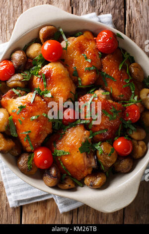 Cosce di pollo arrosto con castagne e i pomodori in una ciotola sul tavolo. verticale in alto vista da sopra Foto Stock