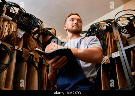 Mechanic rivedendo le scorte in magazzino per spazio di archiviazione Foto Stock