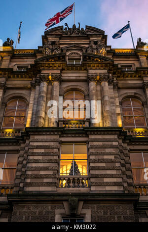 Edificio in stile vittoriano Bank of Scotland quartier generale, il tumulo, accesa fino al crepuscolo con albero di Natale nella finestra e bandiere, Edimburgo, Scozia, Regno Unito Foto Stock