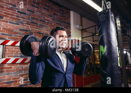 Imprenditore facendo dumbbell bicipite indossare tuta formale. Foto Stock