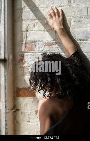 Vista posteriore di una donna triste mano sulla parete mediante la finestra Foto Stock