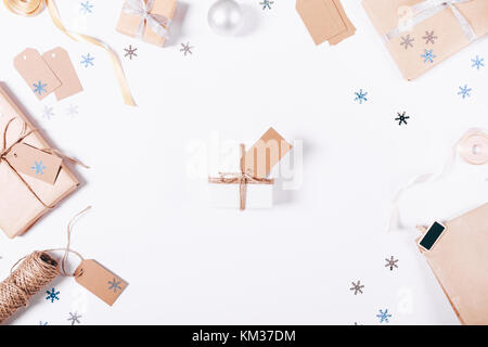 Piccola confezione regalo con un inchino e una etichetta su un tavolo bianco tra le decorazioni di Natale, vista dall'alto Foto Stock