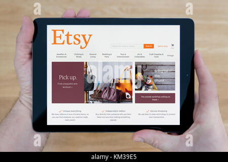 Un uomo guarda il sito Etsy sul suo iPad dispositivo tablet, sparato contro un tavolo di legno top sfondo (solo uso editoriale) Foto Stock