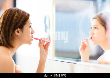 Giovane donna spazzolatura dei denti e guardando nello specchio
