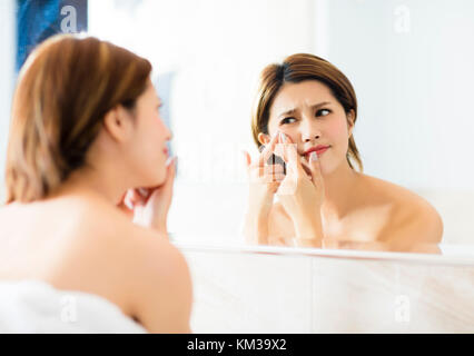 Giovane donna spremere la sua acne davanti allo specchio