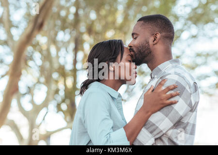 Romantico giovane africano di baciare la sua ragazza di fronte all'aperto Foto Stock