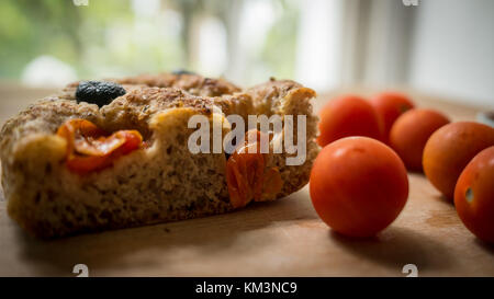 In prossimità di una sezione di una tipica focaccia pugliese su una tavola di legno con pomodori ciliegia. Formato orizzontale. Foto Stock