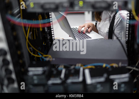 Ritratto di giovane moderno donna portatile tenuta in piedi in sala server lavora con supercomputer Foto Stock