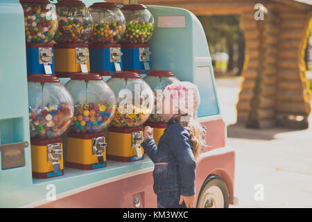 La bambina fermato davanti a una batteria di macchine per la vendita di piccoli dolci. realmente gode di opportunità di scegliere qualsiasi trattamento ritratto di Foto Stock