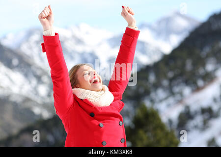 Excited donna indossa una giacca rossa i bracci di sollevamento in una montagna innevata in inverno Foto Stock