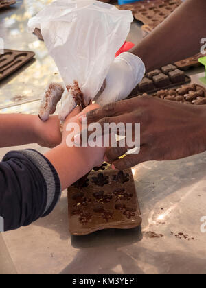 Stretta di mano del colore (adulti) che supporta un bambino è la mano per effettuare piccoli cioccolatini con l'utilizzo della sacca di tela da pasticceria. stampi in gomma con varie forme Foto Stock