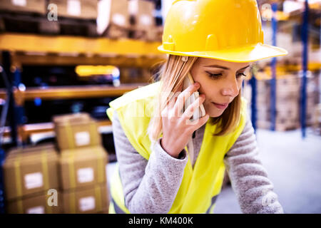 Female warehouse worker with smartphone. Foto Stock