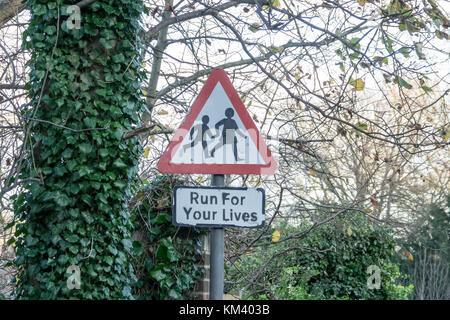 I bambini di avvertimento di attraversamento strada segno con aggiunta di segno unoffical con testo Esegui per la vostra vita, nella cittadina rurale nel Sussex, Inghilterra. Foto Stock