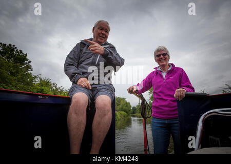 Un uomo si siede nella parte posteriore di un narrowboat mentre una donna sterza con il timone, Trent & Mersey canal, Staffordshire, Inghilterra Foto Stock