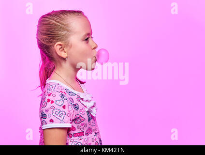 Bambina gonfia un bubble gum su un sfondo rosa Foto Stock