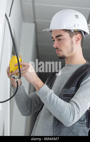 Elettricista misurando la tensione della presa nel nuovo edificio Foto Stock