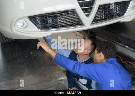 Workshop dipendenti che lavorano insieme sotto un auto sollevato Foto Stock