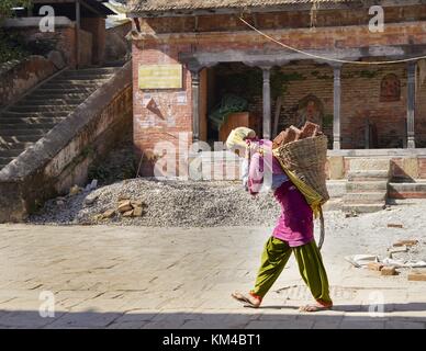 Una giovane donna indossa molti mattoni pesanti sulla schiena nel tempio Changu Narayan vicino a Bhaktapur. (24 novembre 2016) | utilizzo in tutto il mondo Foto Stock