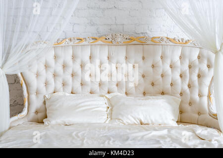 Camera da letto in tenui colori chiari. Grande letto matrimoniale in elegante camera classic. Il lusso elegante colore bianco con oro interior design. Foto Stock