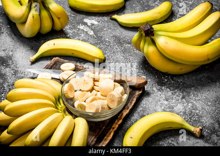 Le banane fresche con pezzi di banane a fettine in una ciotola. su sfondo rustico. Foto Stock