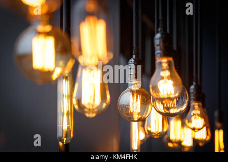 Vintage a filamento di tungsteno a lampade multiple di diverse dimensioni e stile che pendevano dal soffitto su fili neri come un concetto di design interno. Energia una Foto Stock