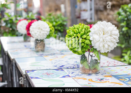 Fake fiori colorati in vasetti di vetro su maiolica decorata in ceramica tavoli, street bar di napoli Foto Stock