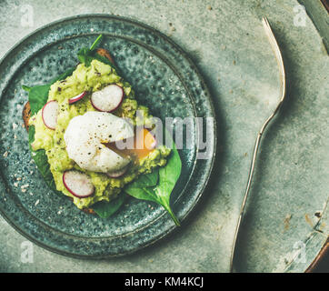 Una sana colazione vegetariana flat-lay. toast integrali con avocado, spinaci, ravanello e Uovo affogato su lastra grigia sfondo, vista dall'alto. La perdita di peso, Foto Stock